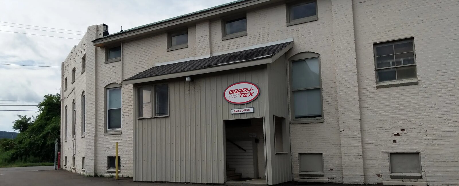 The Graph-Tex facility at 46 Elm Street in Cortland, New York — a white painted brick building with the red Graph-Tex oval above the sales office entrance