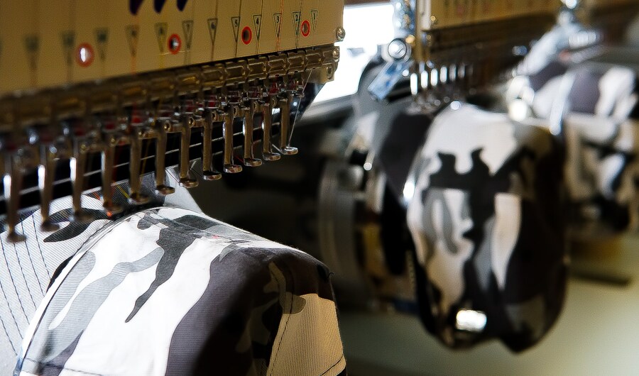 A multi-head commercial embroidery machine running a row of camouflage caps