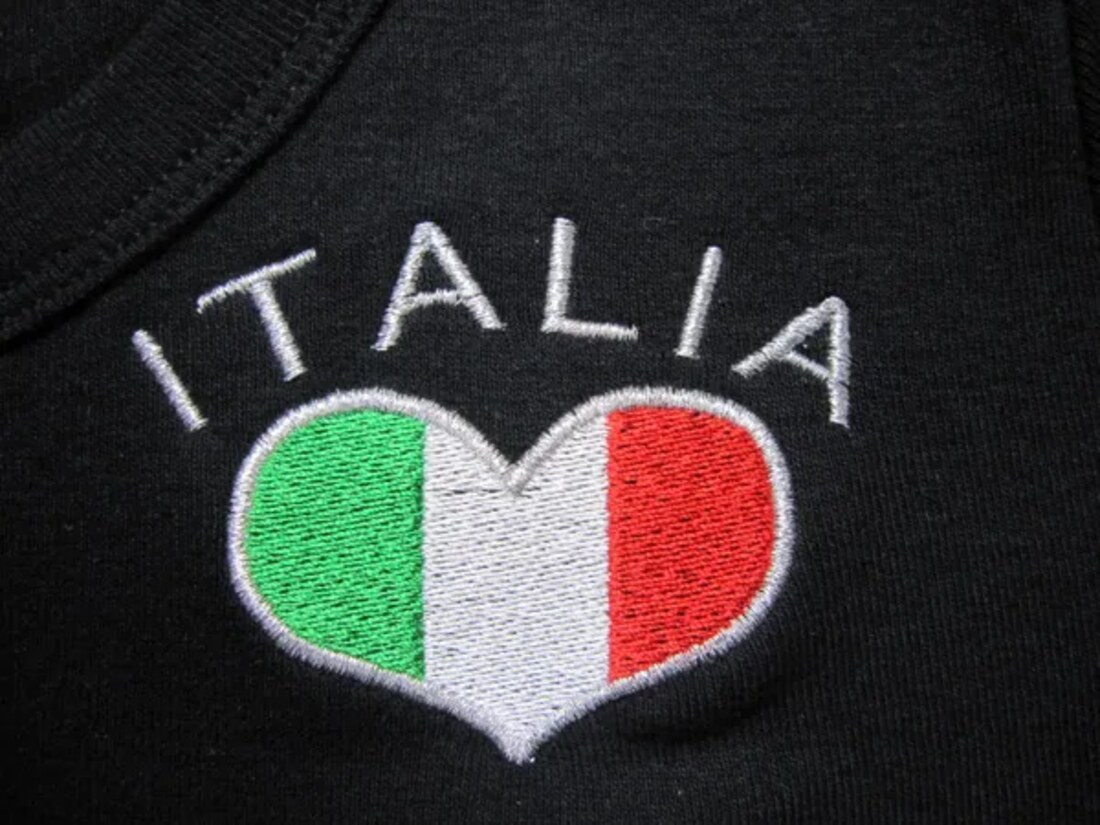 Close-up of embroidery on a black garment — the word ITALIA above a stitched heart in the Italian flag colours